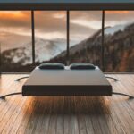 Un lit moderne au centre d'une salle aux grandes fenêtres donnant sur des montagnes