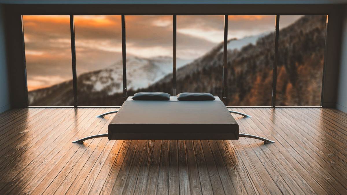Un lit moderne au centre d'une salle aux grandes fenêtres donnant sur des montagnes