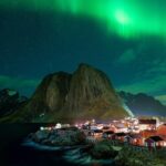 Village illuminé sous les aurores boréales, montagnes et ciel étoilé