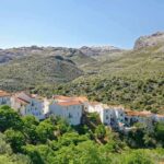 Village blanc aux toits orangés au pied de montagnes boisées sous ciel bleu