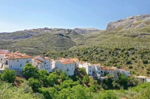 Village blanc aux toits orangés au pied de montagnes boisées sous ciel bleu