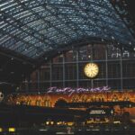 Intérieur d'une gare avec un toit en verre, une horloge, des lumières et des inscriptions