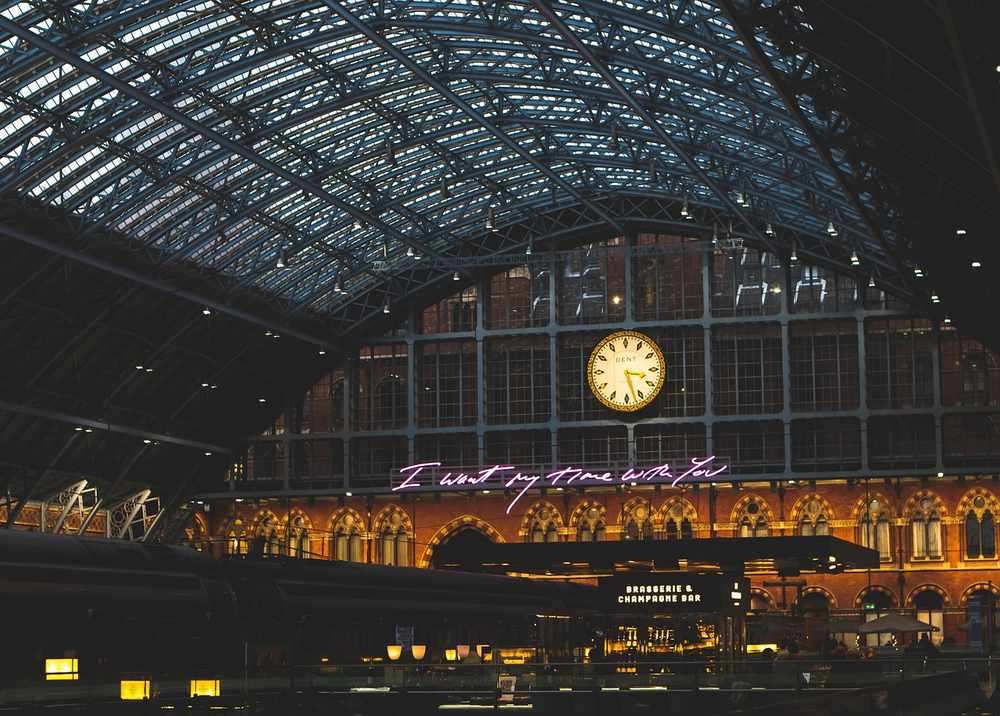 Intérieur d'une gare avec un toit en verre, une horloge, des lumières et des inscriptions