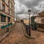 Une rue pavée en pente avec immeubles, lampadaire et ciel nuageux