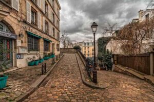Une rue pavée en pente avec immeubles, lampadaire et ciel nuageux